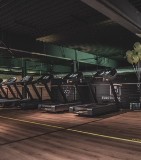 The gym at Dosti West County features modern fitness equipment with treadmills lined up in front of large windows overlooking the property, signifying a well-equipped facility for residents of Thane's Dosti Balkum.